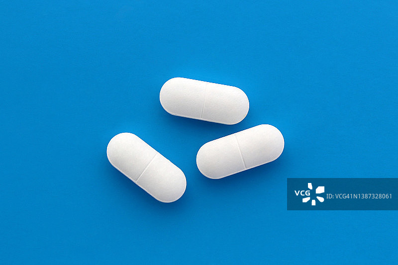 三个长方形的白色药丸躺在蓝色的背景上。从以上观点。图片素材