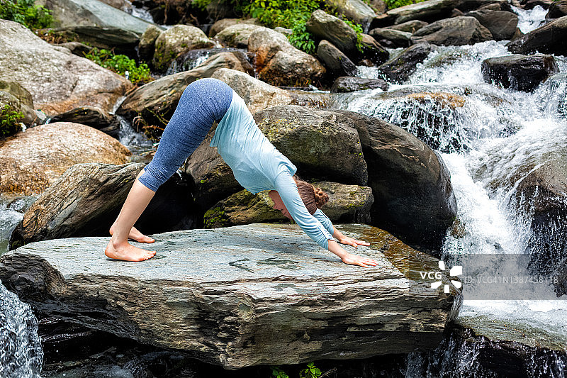 一个年轻的女子在瀑布边做瑜伽图片素材