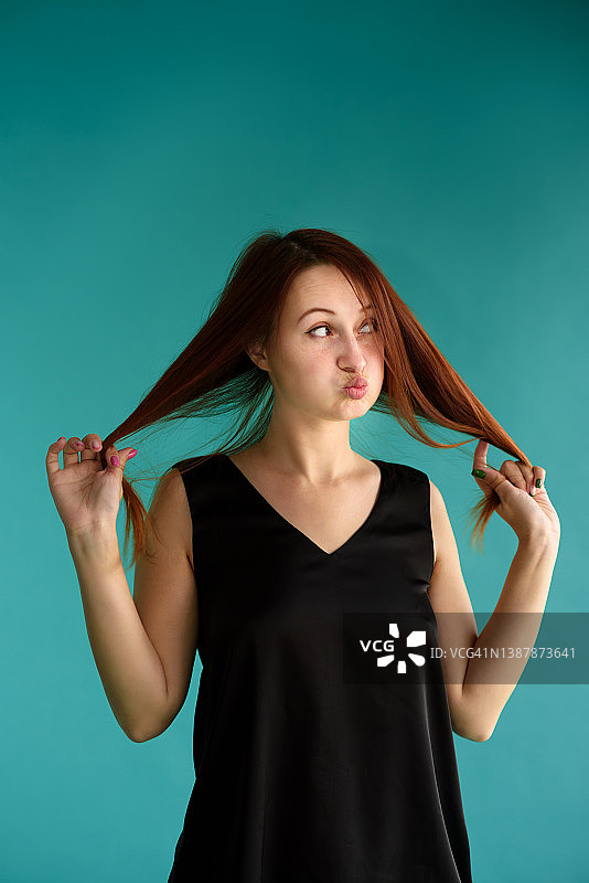长发的年轻女子的肖像与她的红头发，而站在蓝色的背景，鼓起脸颊和开玩笑。图片素材
