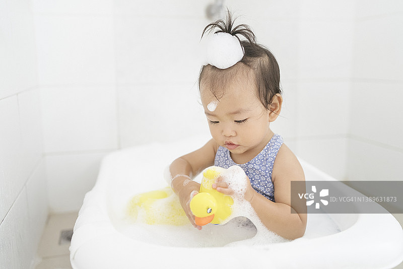 亚洲小女孩在浴室用浴缸里的洗发水洗头的特写镜头。图片素材