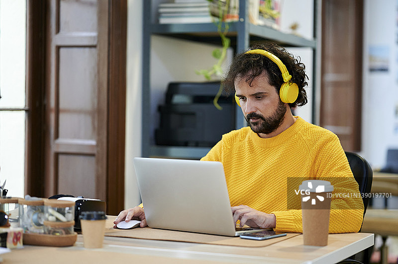 商务人士戴着耳机在办公室用笔记本电脑听音乐图片素材