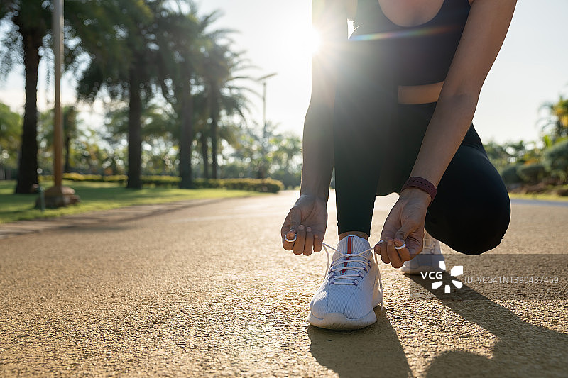 跑步鞋。女人系鞋带。女性运动健身跑步者准备在夏末或秋天的森林小路上慢跑的特写。慢跑是女孩锻炼的动力，健康和健身。图片素材
