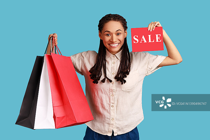 一名女子拿着购物袋，展示促销卡，在商场里宣传低价。图片素材