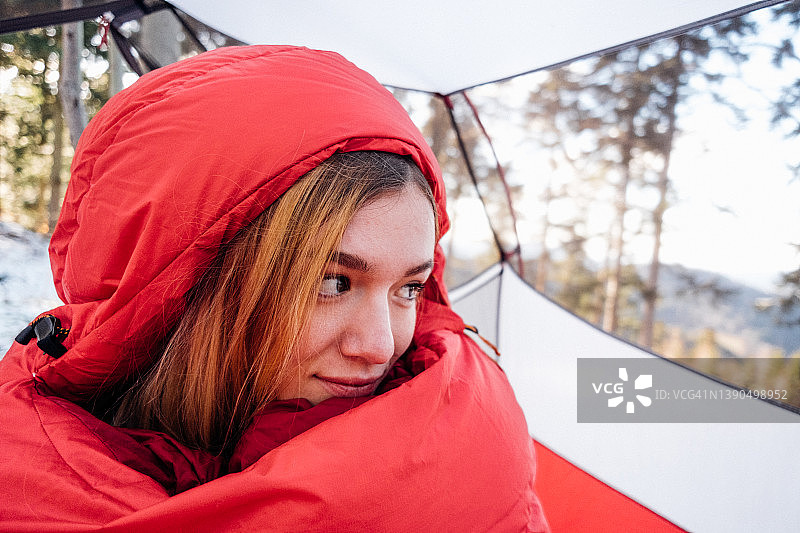 一个裹着红色睡袋的女人向帐篷外张望图片素材