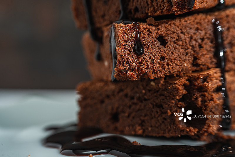 一堆巧克力布朗尼的特写镜头，巧克力丝落在一个白色的盘子和黑色的背景上。图片素材