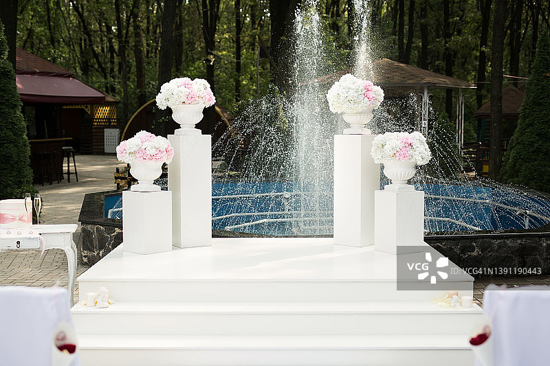 在婚礼的拱形阶段与花卉背景的喷泉。图片素材