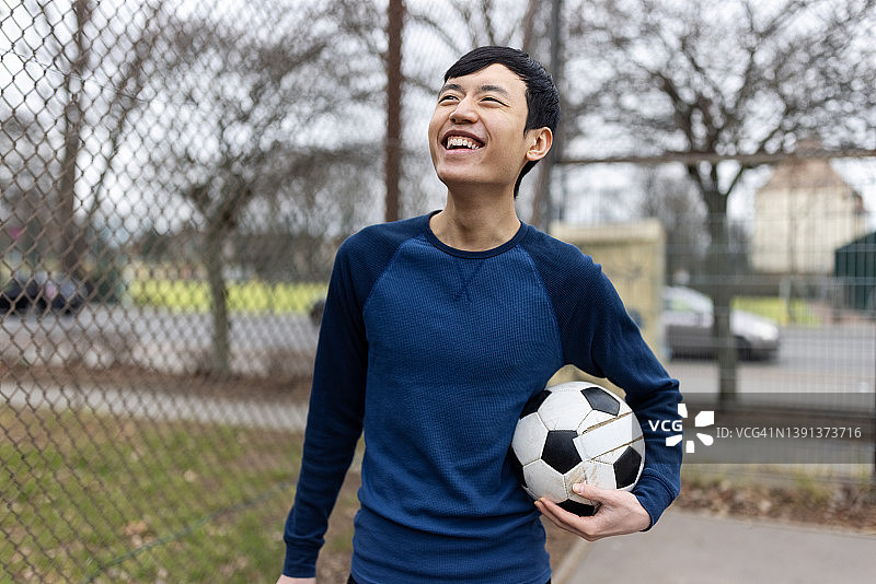 微笑着的中国年轻人在运动场上拿着足球图片素材