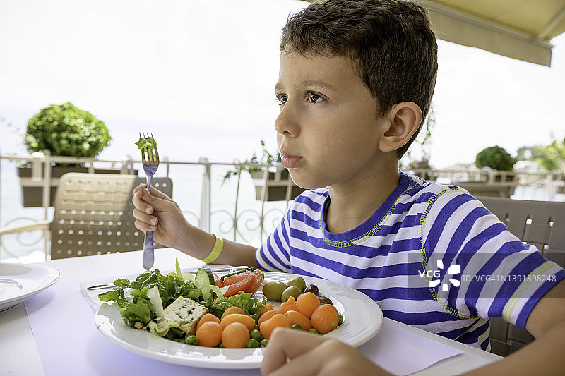 男孩正在餐馆吃蔬菜。图片素材