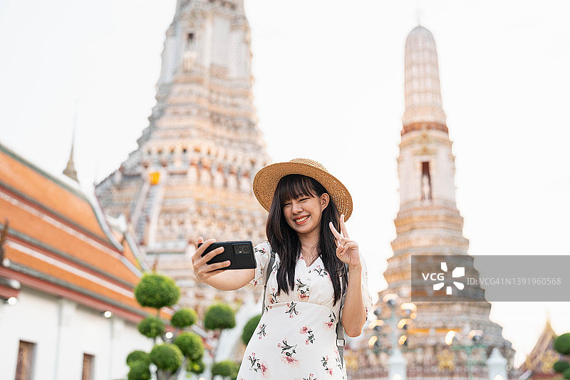 年轻的亚洲女子在曼谷的寺院旅行，用她的智能手机拍照和自拍。图片素材