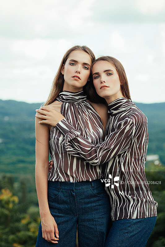 两个欧洲年轻的双胞胎姐妹在大自然的背景下拥抱着看镜头图片素材