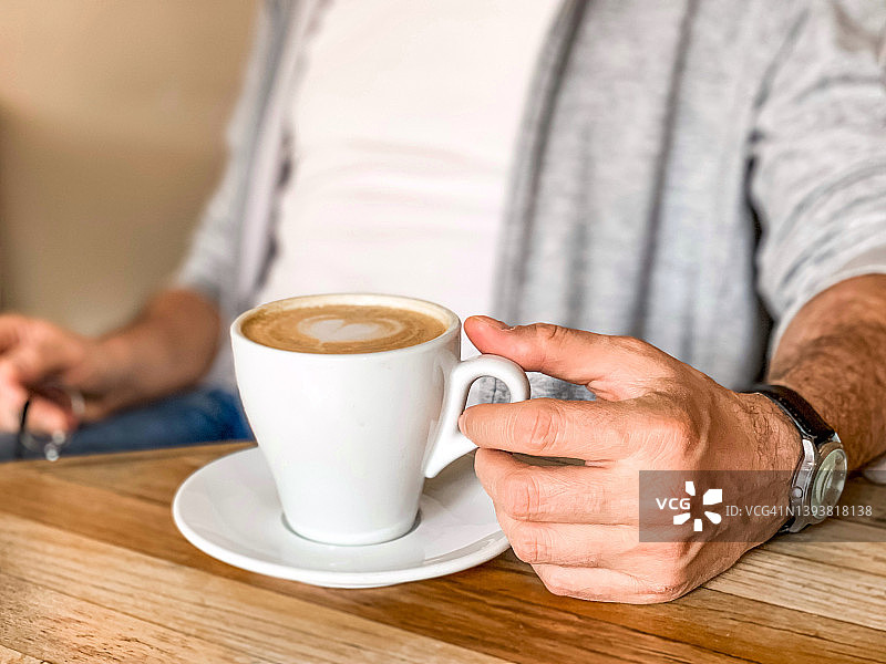 年轻人正在喝咖啡在咖啡馆白色陶瓷杯与茶托在木桌图片素材