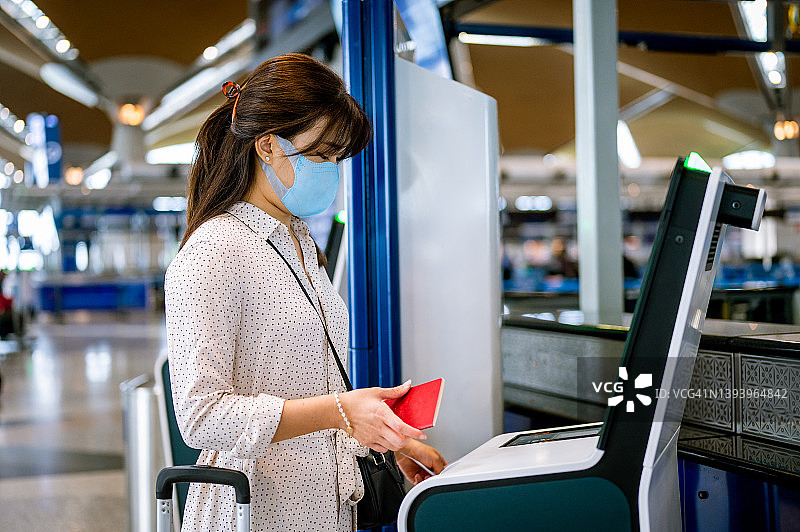 一名戴着口罩在机场办理登机手续的亚洲女性旅客正在办理登机牌图片素材