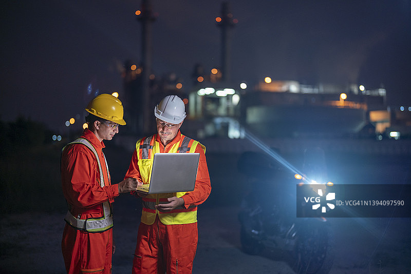 两名工程师上夜班，在一家石油工厂前使用技术。图片素材