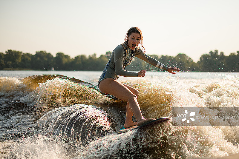 在一个温暖的日子里骑在溅起水花的波浪上冲浪的惊讶湿女人图片素材