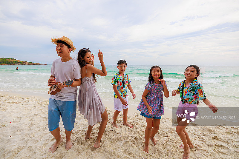 亚洲父亲和他的家人在海滩上弹吉他。度假和放松的概念。图片素材