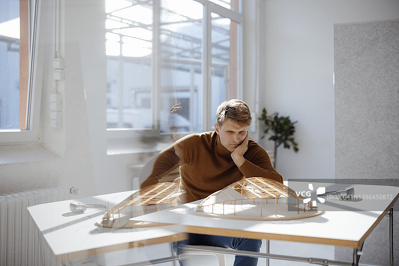 建筑师坐在办公室用手看树叶形状的模型图片素材