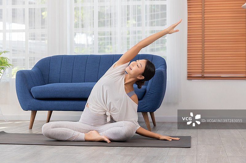 女性在家做伸展运动，坐在垫子上的侧角姿势，瑜伽锻炼。图片素材