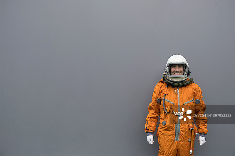 宇航员穿着橙色宇航服和头盔站在灰色的墙壁背景图片素材