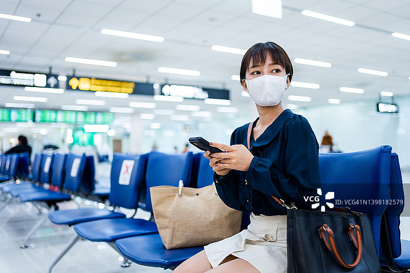 一名亚洲年轻女子在机场候机楼等待航班起飞时使用手机。图片素材