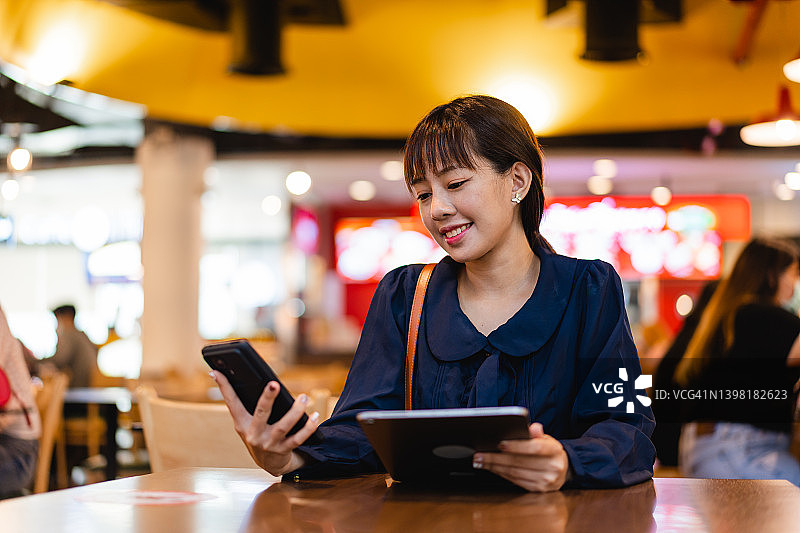 一名亚洲年轻女子在机场候机楼的美食区使用电子平板电脑图片素材