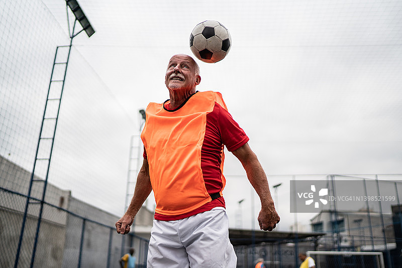年长的男子跳着用他的头在足球场击球图片素材