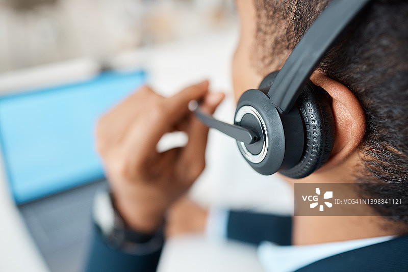 混合种族的男性呼叫中心代理，在工作时戴着耳机接听电话。一位西班牙商人在办公室的办公桌前讲电话图片素材
