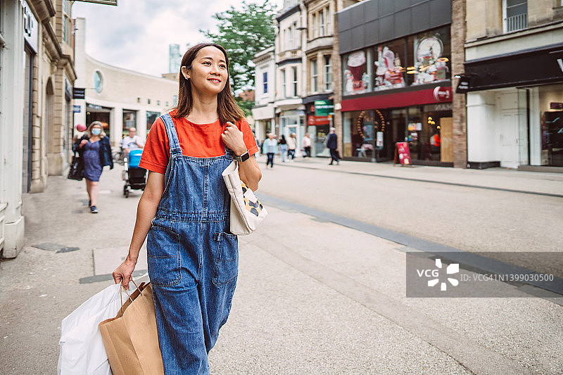 年轻开朗的亚洲妇女提着购物袋走在商业区的大街上图片素材