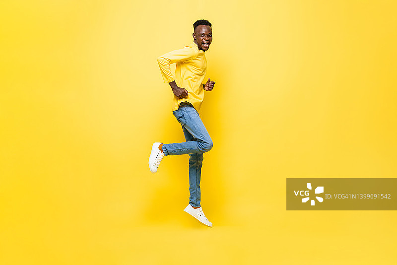 全长肖像兴奋的非洲人跳跃在孤立的黄色工作室背景图片素材