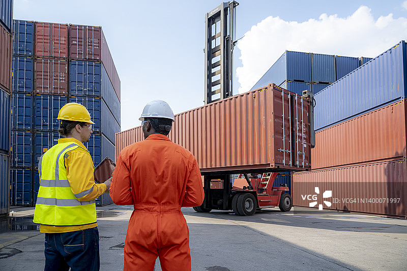 两名工人对货物集装箱进行讨论，控制从货物运输船上装载集装箱图片素材
