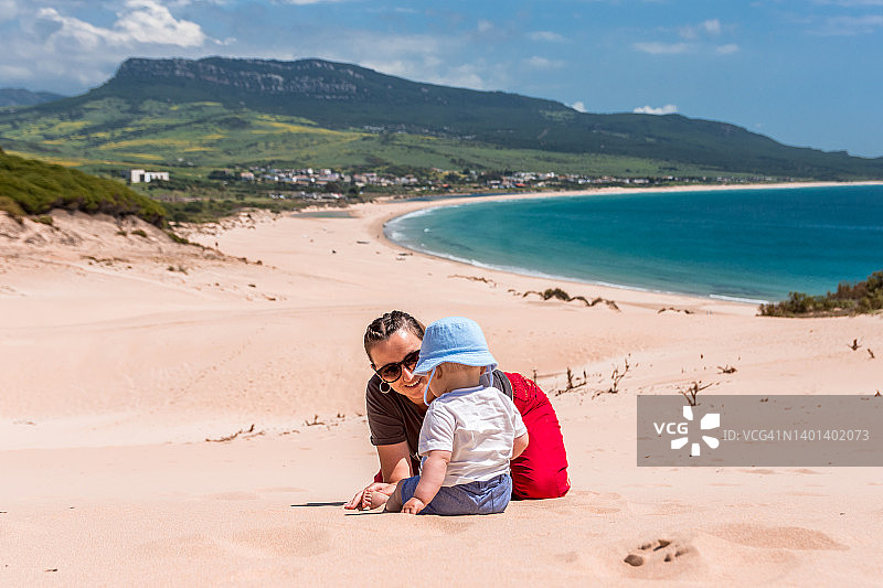 妈妈和她的孩子在沙滩上玩耍。蓝天和天堂海滩的背景。图片素材