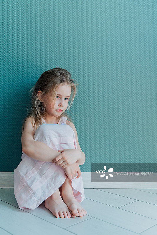 小伤心沮丧的金发女孩穿着白裙子坐在室内的地板上。本空间图片素材