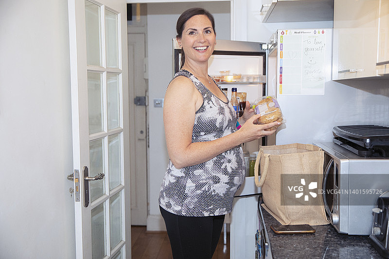 肖像快乐的孕妇正在厨房里收拾食品杂货图片素材