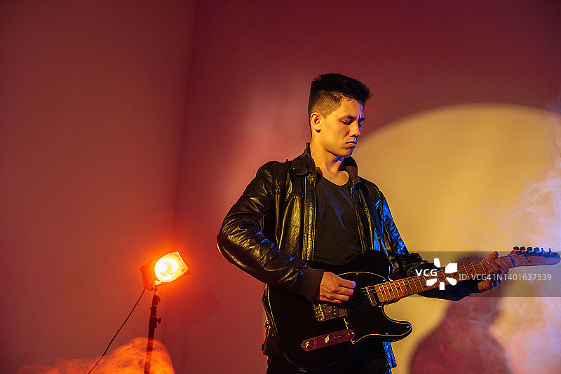 美丽的亚洲男子吉他手在霓虹灯下与复制空间的吉他上演奏和享受音乐图片素材