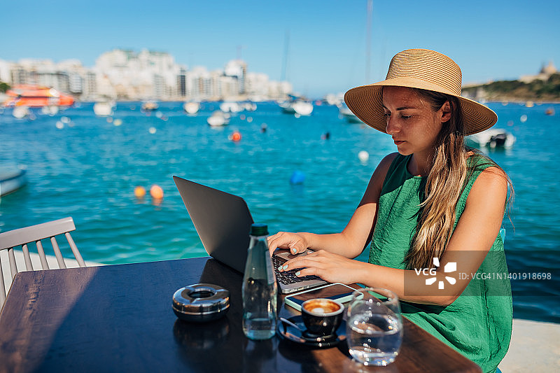 一位女性自由职业者坐在海边的咖啡店里使用笔记本电脑图片素材