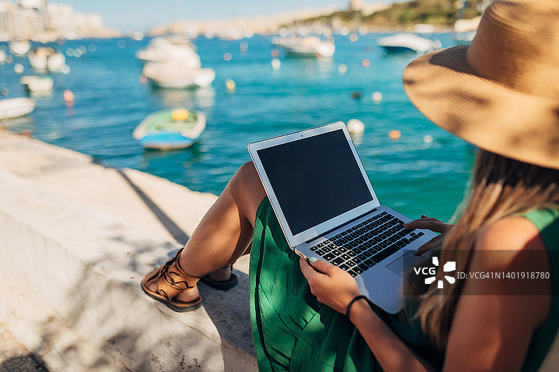一个女人的后视图享受大海和海港的景色，同时使用笔记本电脑远程工作图片素材