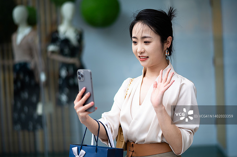 亚洲年轻美丽的女人拿着购物袋和智能手机在城市街道图片素材