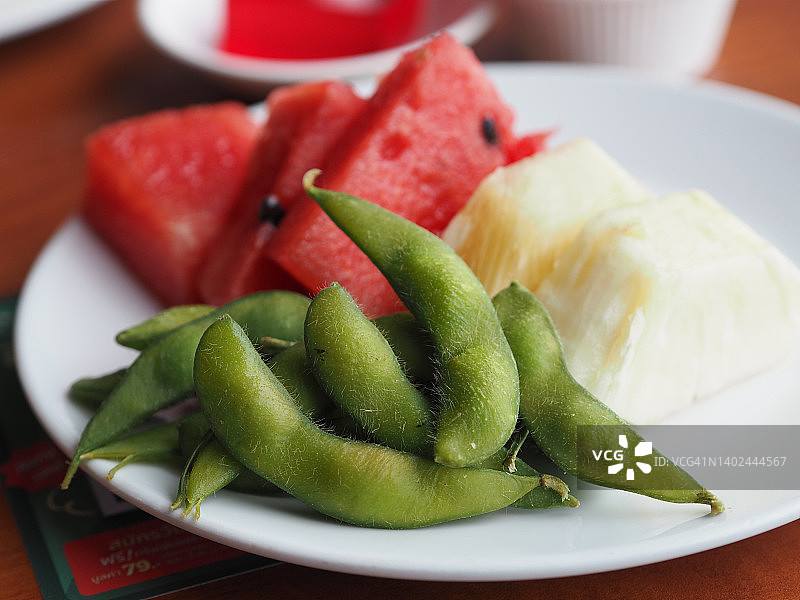 毛豆，菠萝，水马龙水果和蔬菜素食在白色盘子木桌子的背景图片素材