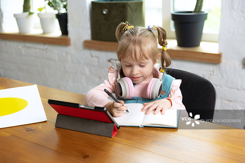 可爱小女孩的真人肖像，学龄前儿童靠在家里使用数码平板电脑。教育、童年、人、作业和学校观念。图片素材