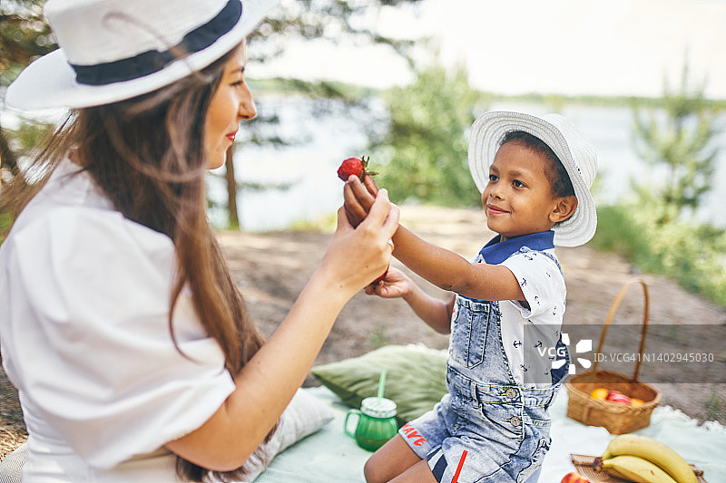 一个4岁的小男孩和他的妈妈在河边野餐，吃浆果和水果图片素材