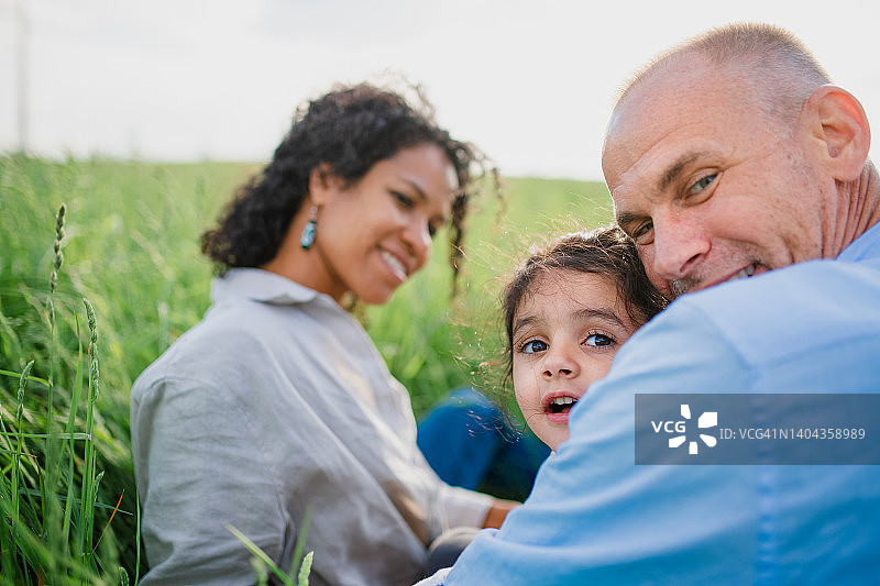 幸福的多种族家庭坐在草地上，微笑着看着镜头。图片素材