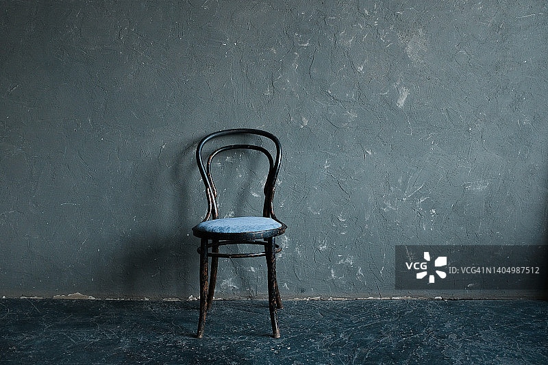 客厅内部有一把木椅或扶手椅，靠着一堵灰色的墙。极简主义的概念。图片素材