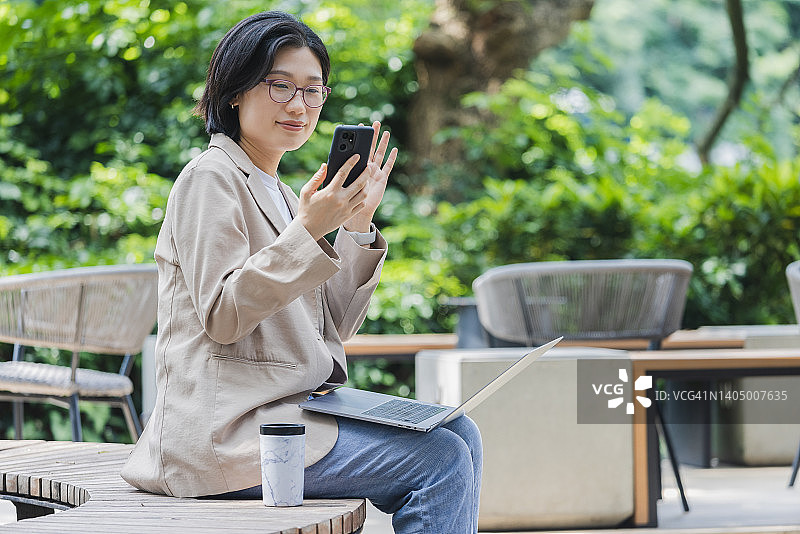 一位在户外咖啡馆里对着手机挥手的亚洲女性图片素材