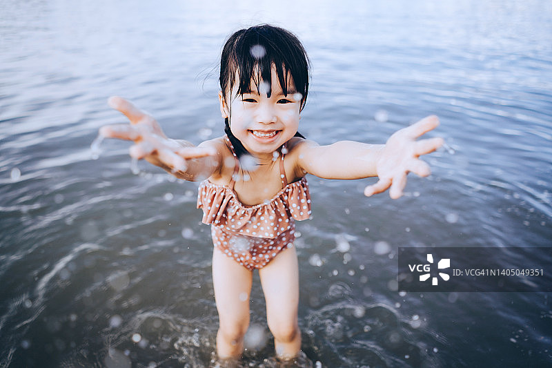 顽皮的亚洲小女孩开心地微笑着，在夏天的海滩上嬉水嬉戏图片素材