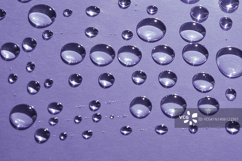 紫色背景上的化妆品精华液、凝胶或雨滴。图片素材