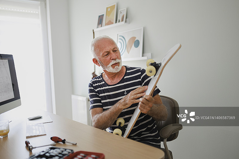 一位老人在家用电脑修理他的滑板，并按照指令操作图片素材