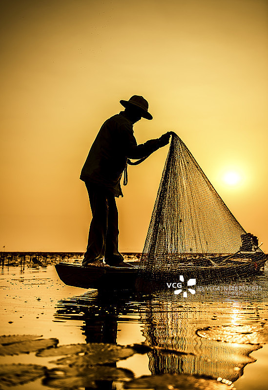 剪影渔夫使用渔网在船上捕鱼。图片素材