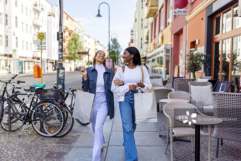 两个女性朋友带着购物袋微笑着走在城市里图片素材