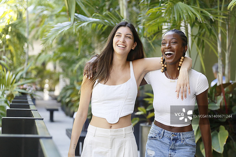一个扎着辫子的非裔美国Z世代女性，和一个留着黑色长发的拉丁x Z世代女性，穿着休闲装穿过购物区。图片素材