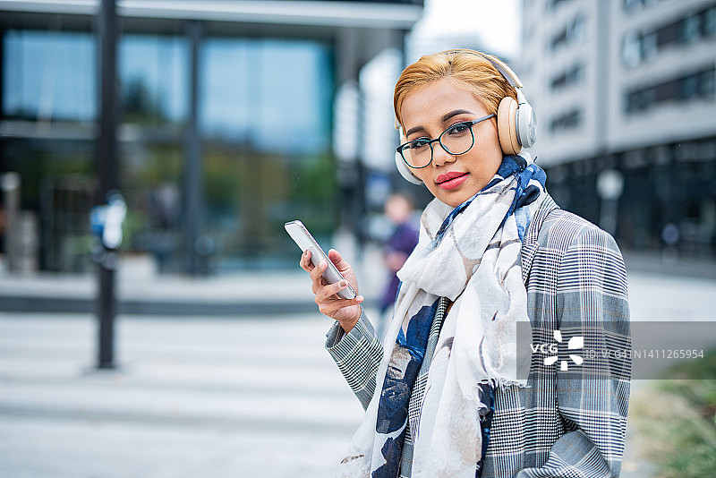 戴着耳机和手机的女人站在城市街道上图片素材
