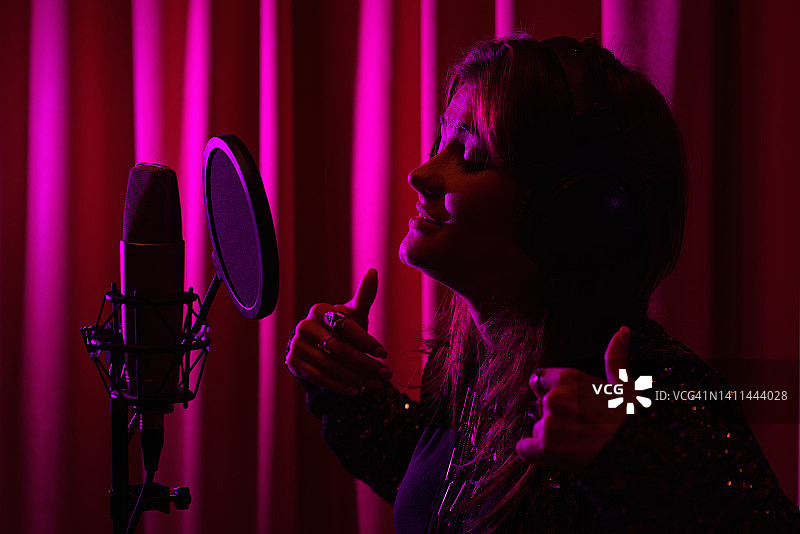 在霓虹灯下用麦克风录制专业音乐工作室歌曲的情感音乐家女性图片素材